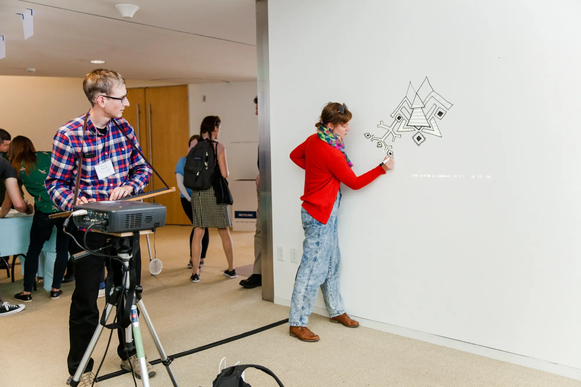 A participant drawing on a wall while another operates a projector at PCD Boston